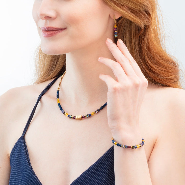 Coeur de Lion beaded necklace, bracelet and earrings in gold and blue colours with purple on model - Carathea & Jools