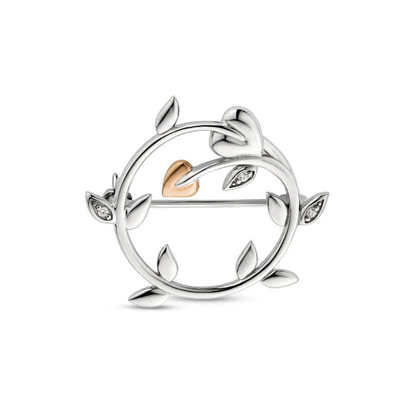 A silver circular leaf brooch with a small rose gold heart at the center and tiny clear stones in several leaf tips, shown on a plain white background.