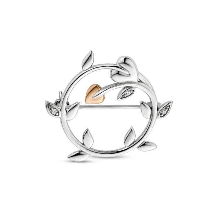 A silver circular leaf brooch with a small rose gold heart at the center and tiny clear stones in several leaf tips, shown on a plain white background.