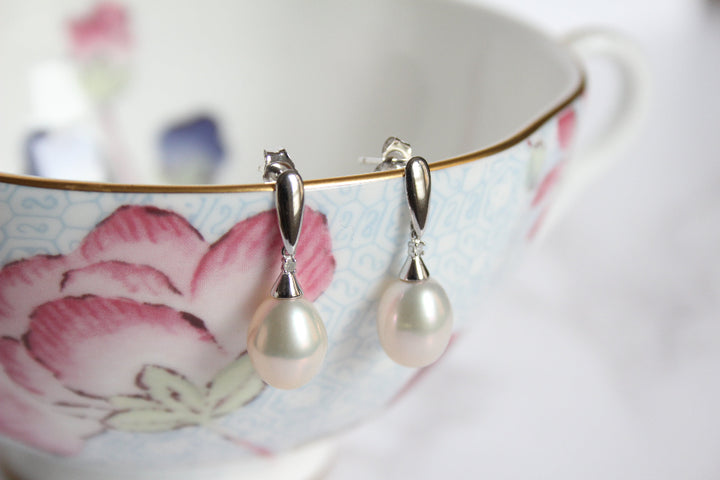 A pair of 9ct white gold drop earrings with diamond and with large white pearl hanging from a light blue floral teacup with pink flowers and gold trim.