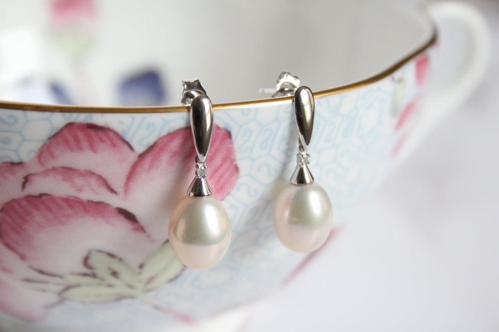A pair of 9ct white gold drop earrings with diamond and with large white pearl hanging from a light blue floral teacup with pink flowers and gold trim.