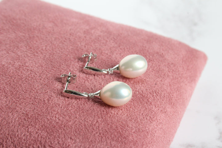 A pair of 9ct white gold drop earrings with diamond and with large white pearl laying on pink cushion - carathea & jools