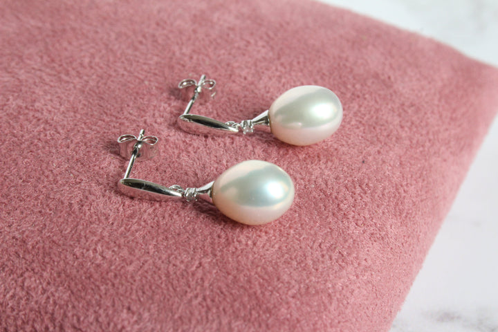 A pair of 9ct white gold drop earrings with diamond and with large white pearl laying on a pink cushion - Carathea & Jools