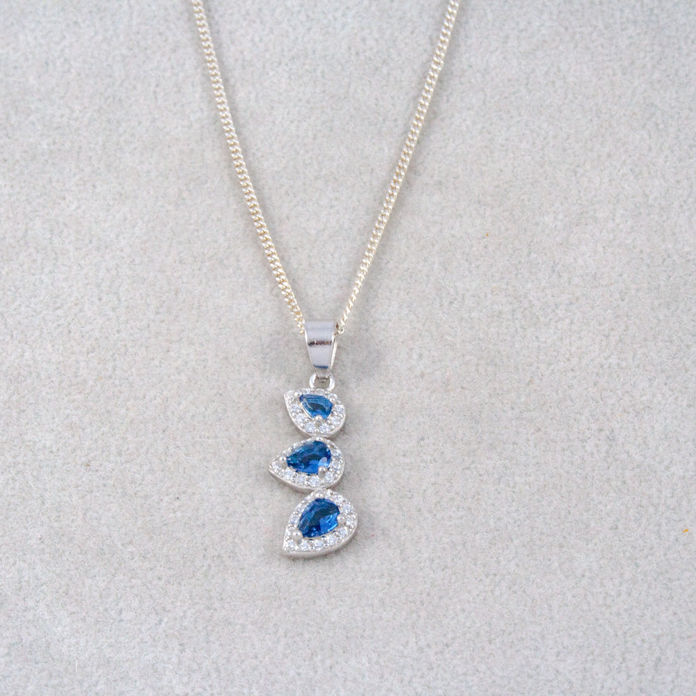 Silver necklace with a pendant featuring blue gemstones on a light gray background