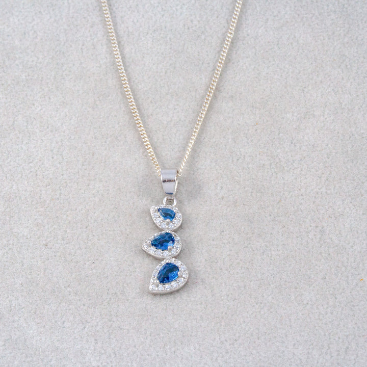 Silver necklace with a pendant featuring blue gemstones on a light gray background