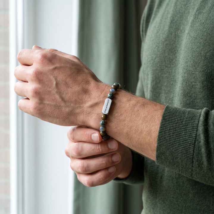 A close-up of a man's wrist wearing a beaded bracelet with a small white rectangular tag that reads 'PINECREEK'.