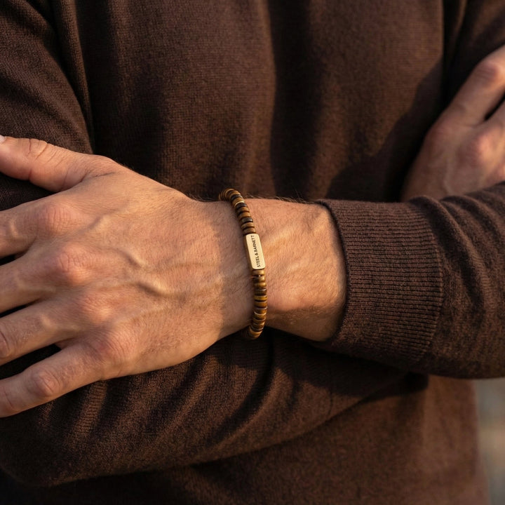 Person wearing a brown Tiger's Euebeaded bracelet with a metal tag on a blurred background