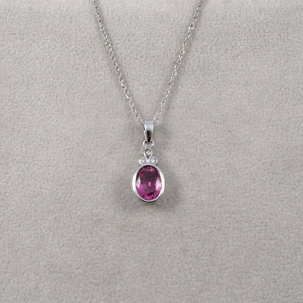 A white gold chain necklace with an oval pink tourmaline gemstone with three diamonds pendant, displayed on a textured light gray background.