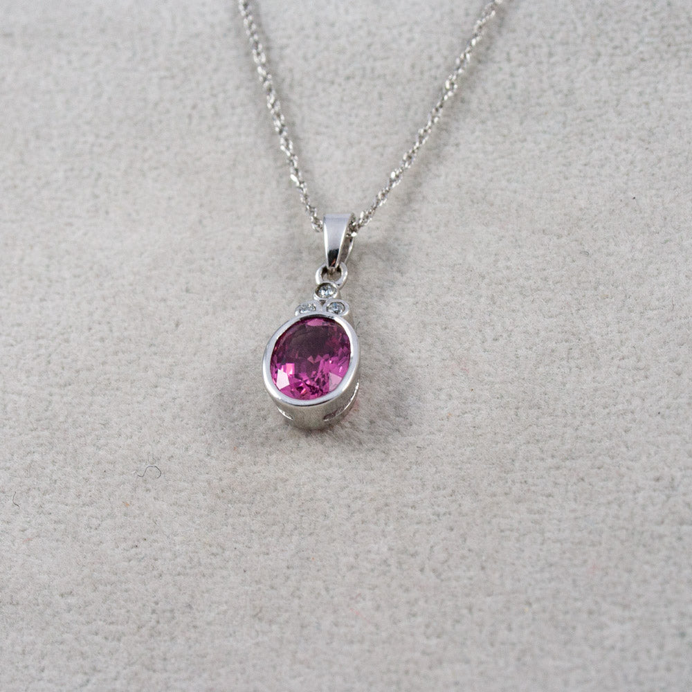 A white gold chain necklace with an oval pink tourmaline gemstone with three diamonds pendant, displayed on a textured light gray background.