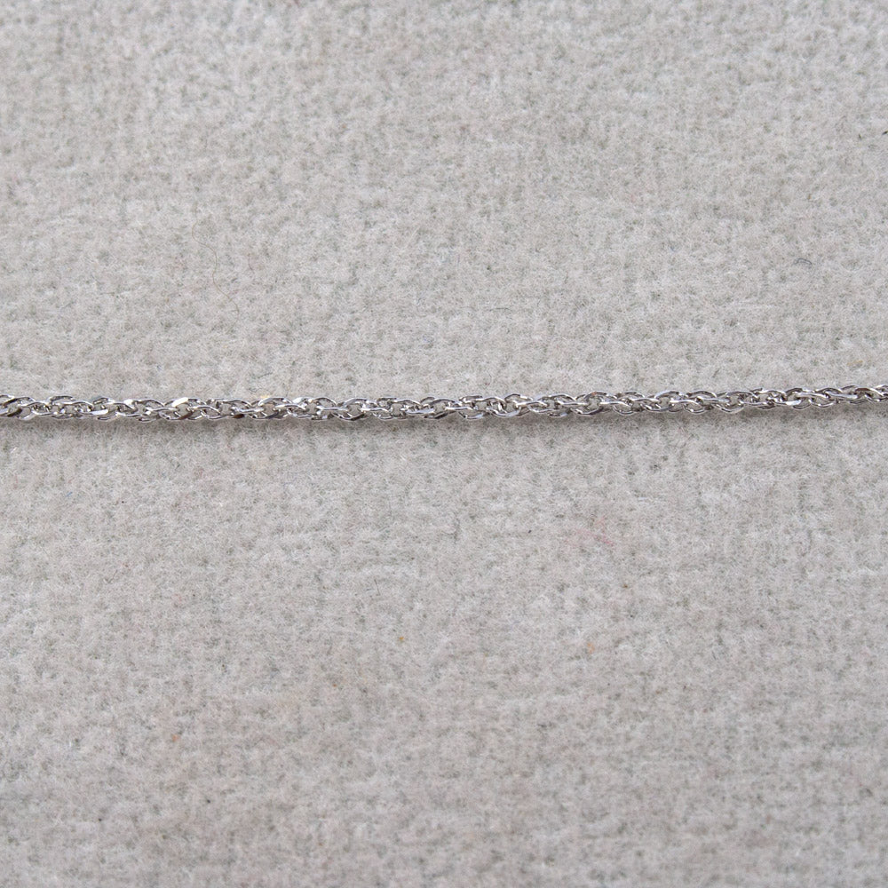 A close-up of a white gold twisted rope chain laid horizontally across a light beige textured surface.