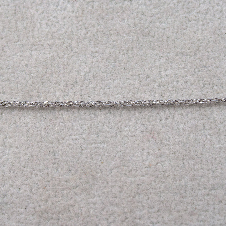 A close-up of a white gold twisted rope chain laid horizontally across a light beige textured surface.