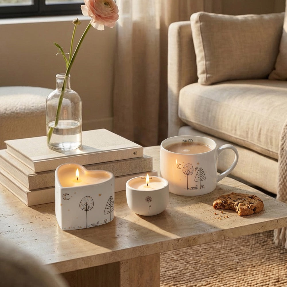 Belly Button Lovely Friend candle in its cream ceramic pot, shown lit on a coffee table with styling props.