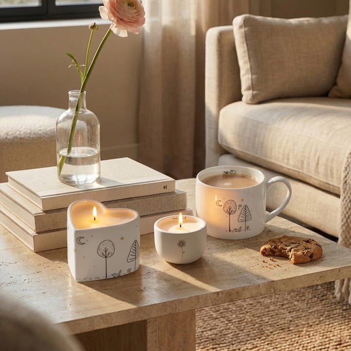 Belly Button Lovely Friend candle in its cream ceramic pot, shown lit on a coffee table with styling props.