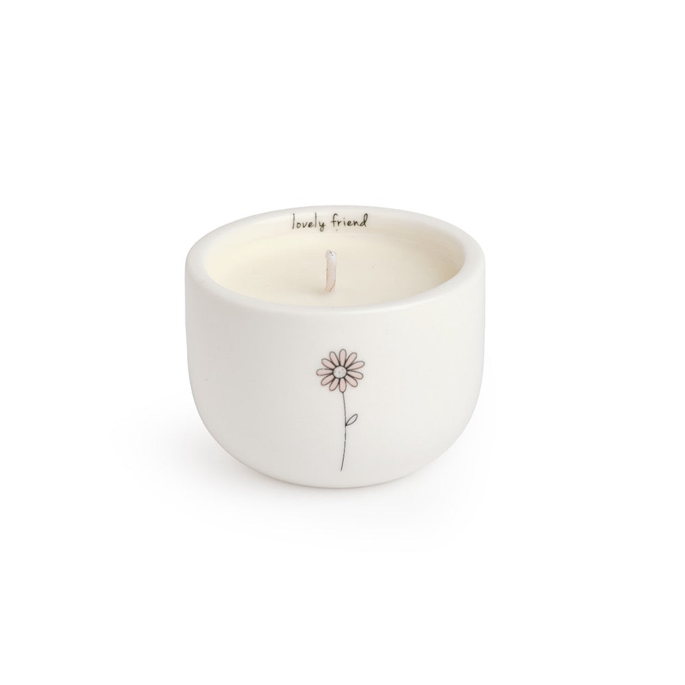 Belly Button Lovely Friend candle in a round cream ceramic pot with its message inside the rim and a pink flower outside.