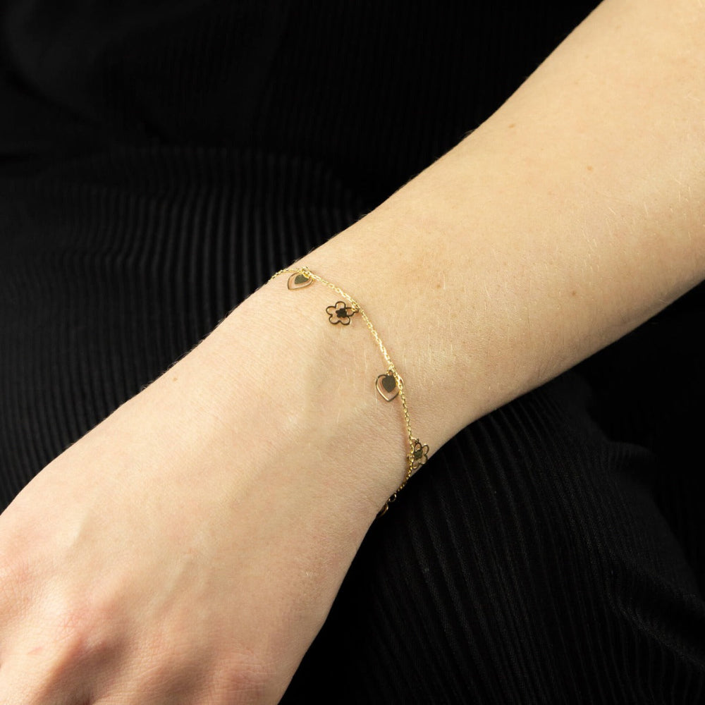 The 9ct gold heart and flower charm bracelet worn on the wrist.