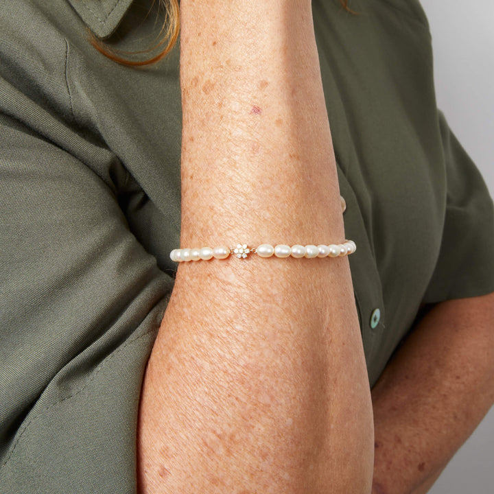 The seed pearl bracelet worn on the wrist, with its small diamond-set gold flower at the front.