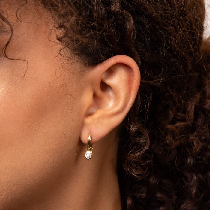 Close-up of an ear wearing a gold hoop earring with a small diamond.