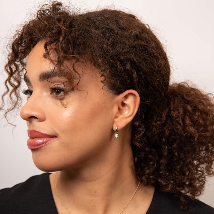 Woman with styled hair against a neutral background with gold hoops with diamond charm dangle