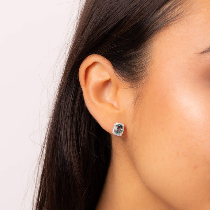 A woman wearing a 9ct white gold stud earring with an oval blue fluorite in a rectangular white topaz halo.
