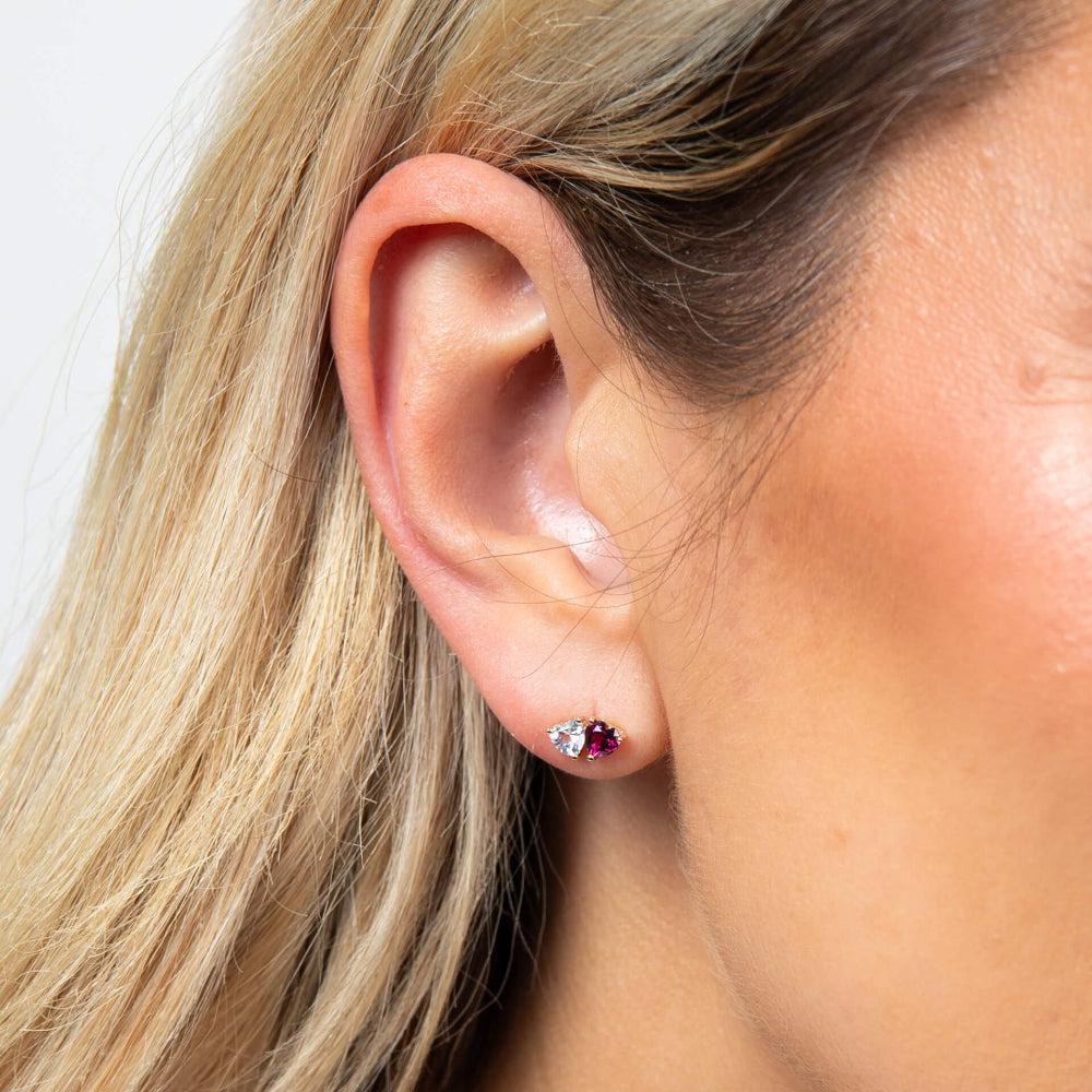 A woman wearing a 9ct yellow gold Toi et Moi stud earring with a white topaz heart and a rhodolite garnet heart.