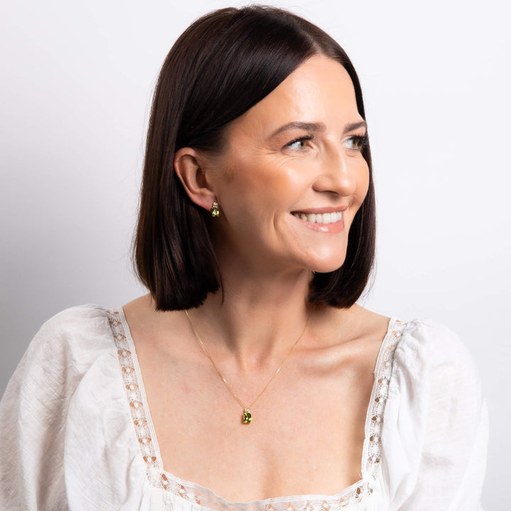 Woman wearing a white blouse with lace details and a peridot necklace and earring set on a plain background