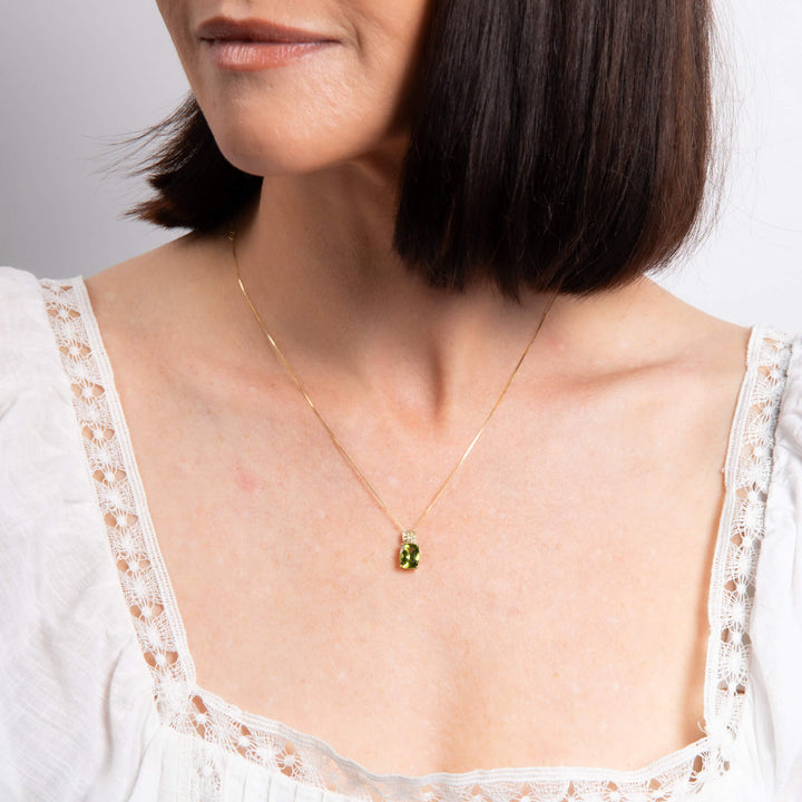 Woman wearing the 9ct yellow gold cushion-cut peridot pendant on a fine gold chain at the neckline.