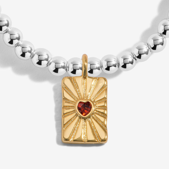 Silver and gold beaded bracelet with a heart charm and red crystal.