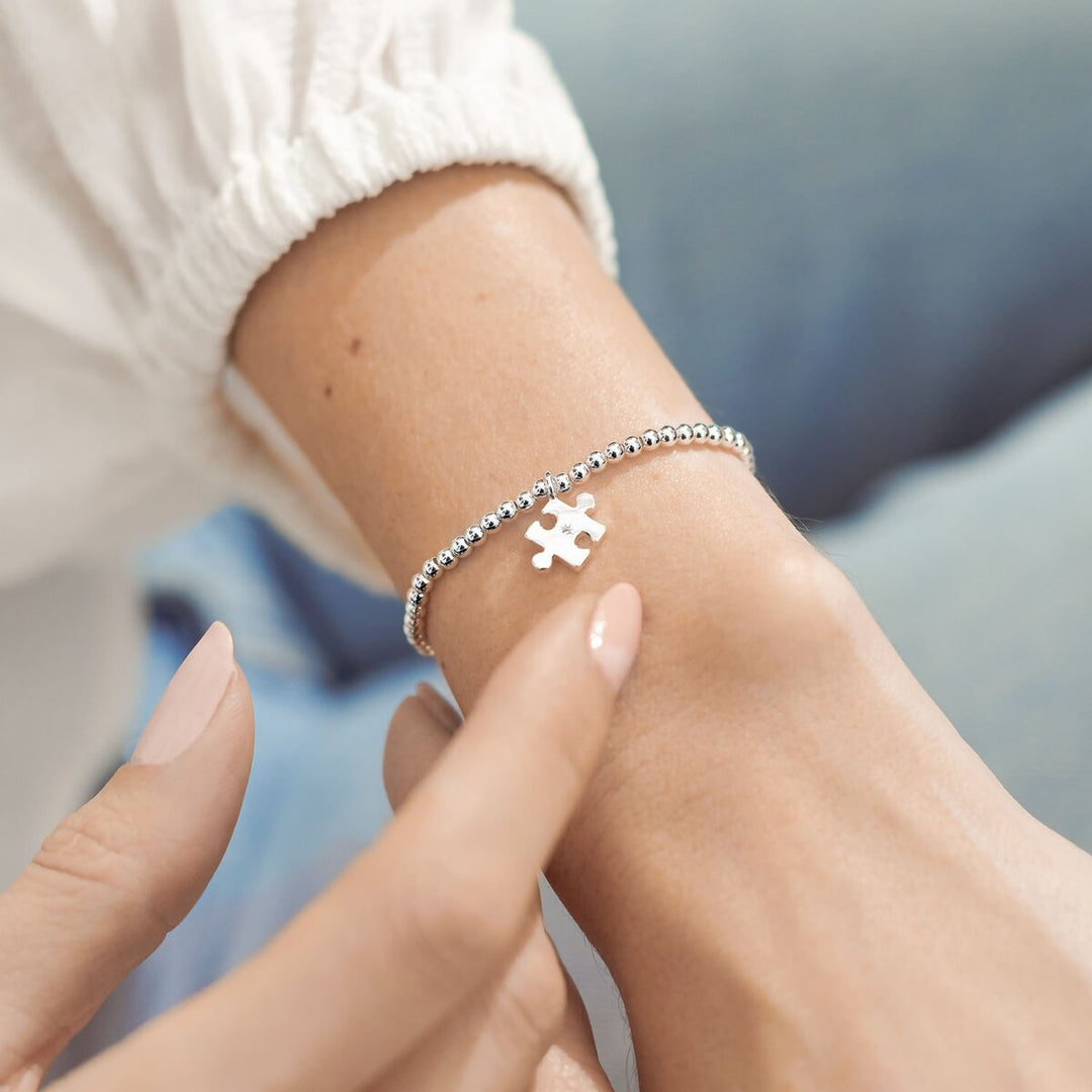 Silver bracelet with a puzzle piece charm on a wrist against a blurred background