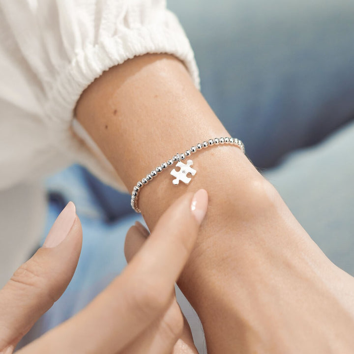 Silver bracelet with a puzzle piece charm on a wrist against a blurred background
