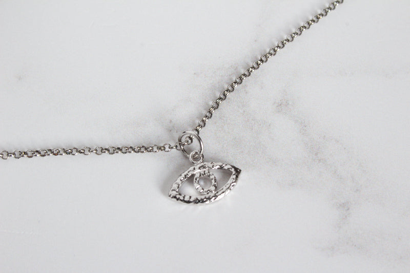 A silver evil eye necklace, displayed on a light gray marble surface.