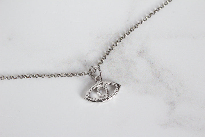 A silver evil eye necklace, displayed on a light gray marble surface.