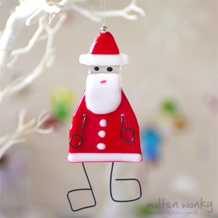 A fused glass Santa ornament hanging from a tree