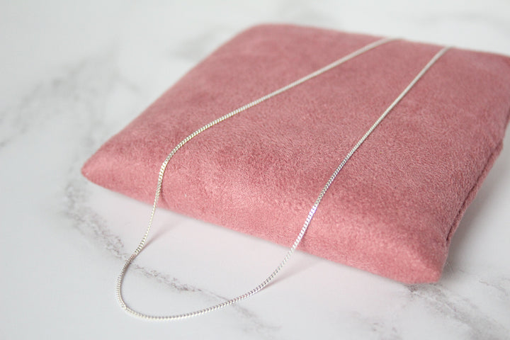A silver curb chain necklace draped over a dusty pink jewelry display pillow on a white marble surface - Carathea & Jools