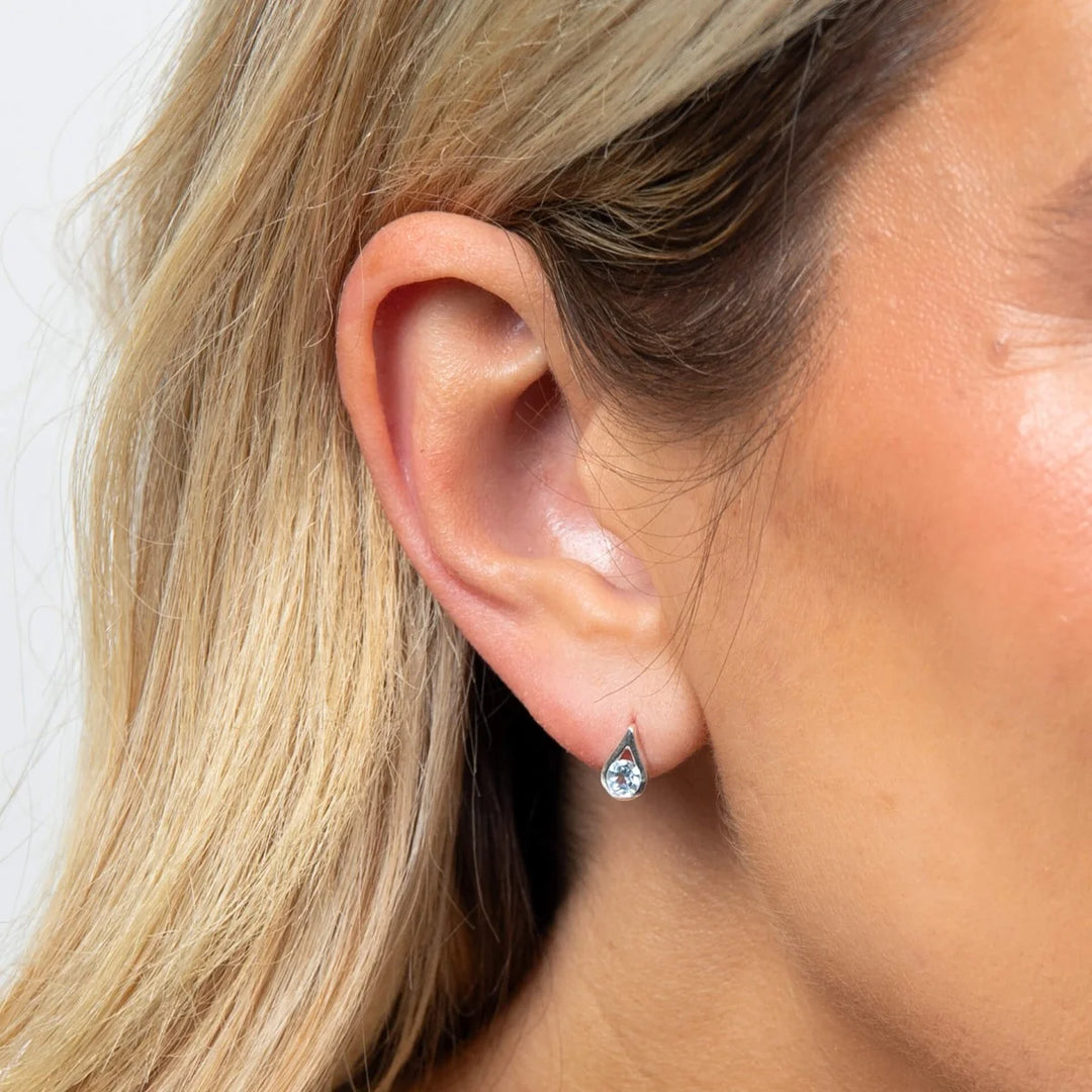 These are polished sterling silver stud earrings with teardrop-cut blue topaz stones, measuring nine by five millimeters | Carathea & Jools