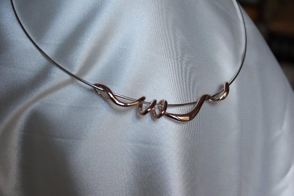A silver torque necklace with rose gold twist detail draped on satin fabric - Carathea & Jools
