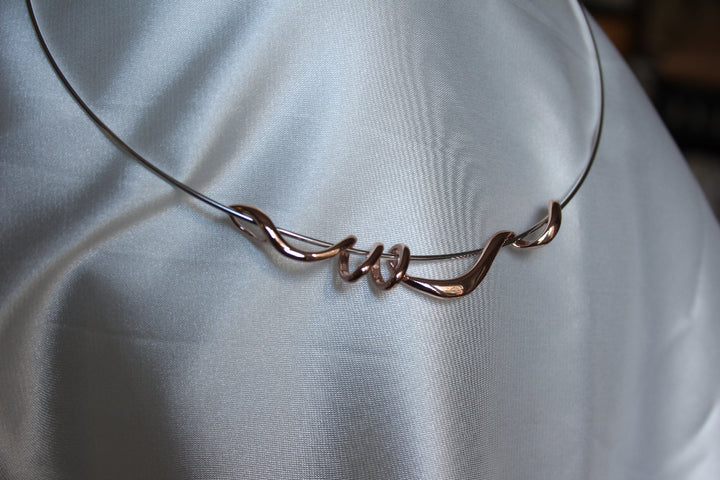 A silver torque necklace with rose gold twist detail draped on satin fabric - Carathea & Jools