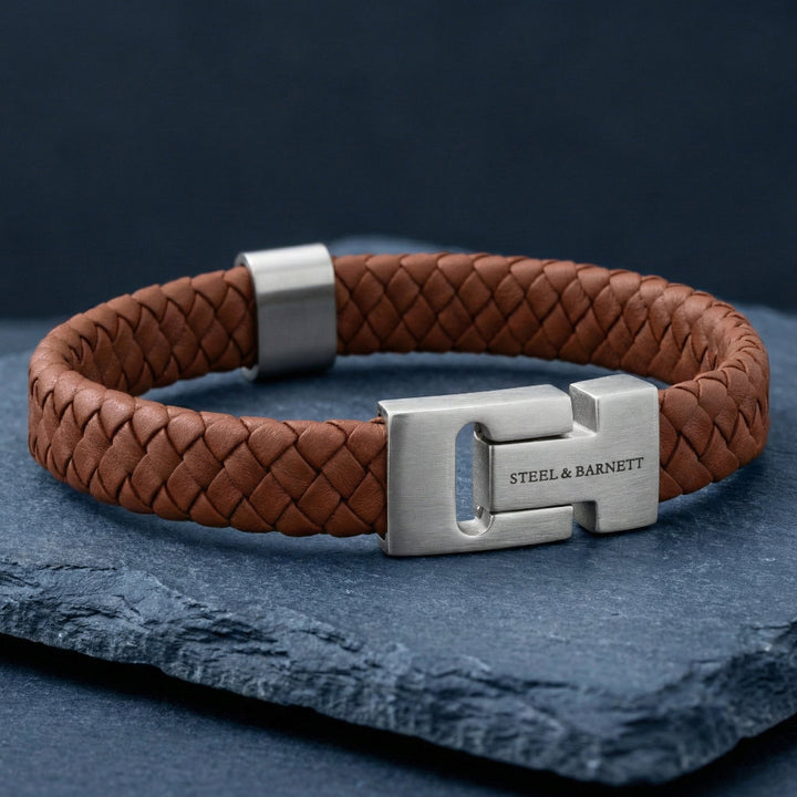 Brown braided leather bracelet with a silver clasp on a dark blue surface