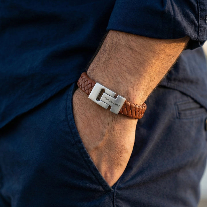 Brown braided bracelet with a silver clasp on a person's wrist, wearing a dark blue shirt.