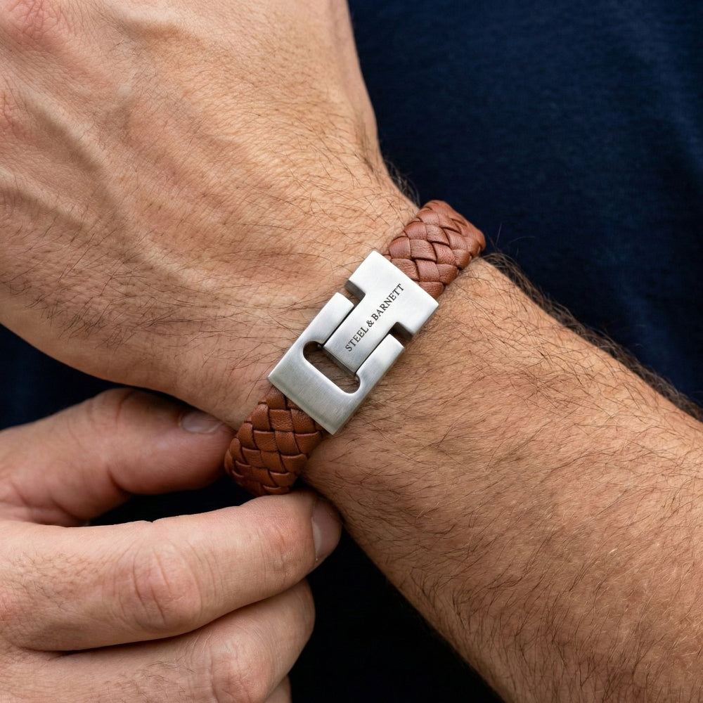 Brown leather bracelet with silver clasp on a wrist, being adjusted by a hand.