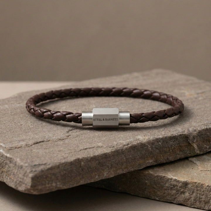 Brown braided leather bracelet with silver clasp on a stone surface