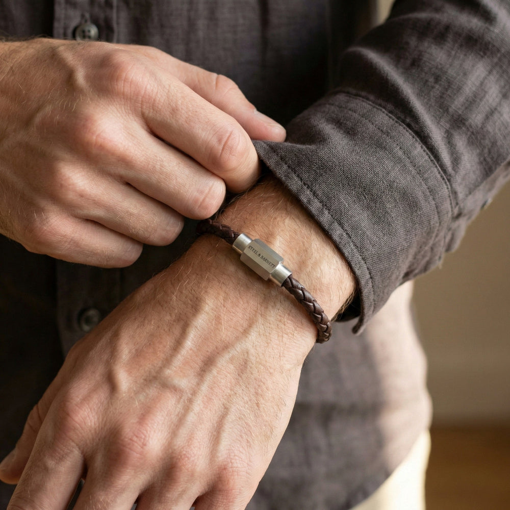 Person adjusting a brown leather bracelet with a metal clasp on their wrist.