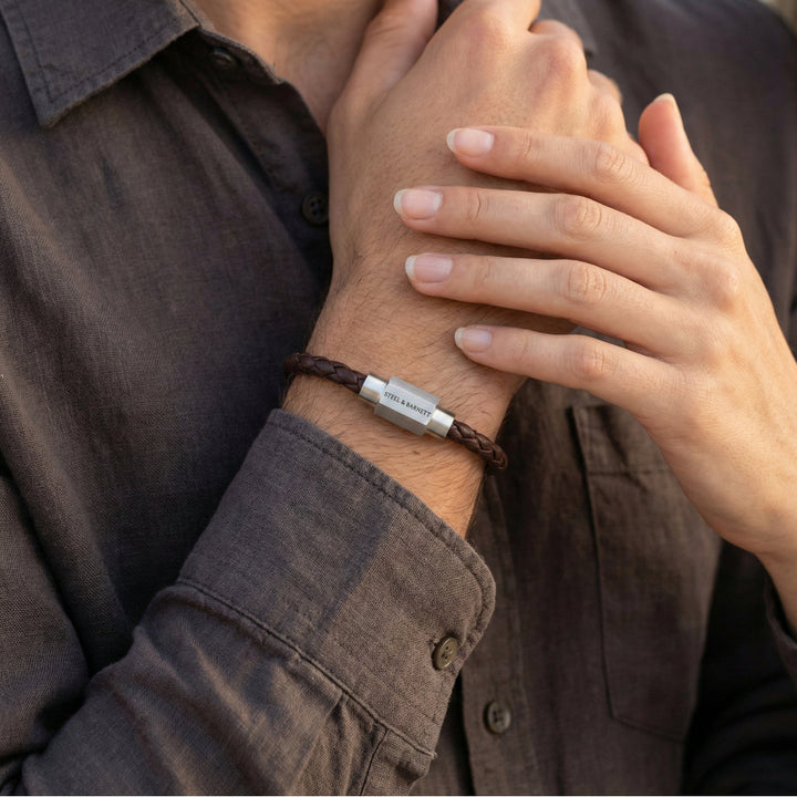 Close-up of a person wearing a leather bracelet with a metal tag, held by another person.