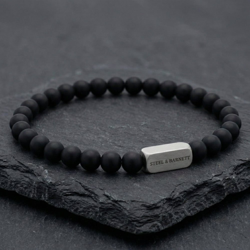 Black beaded bracelet with a silver tag on a dark stone surface