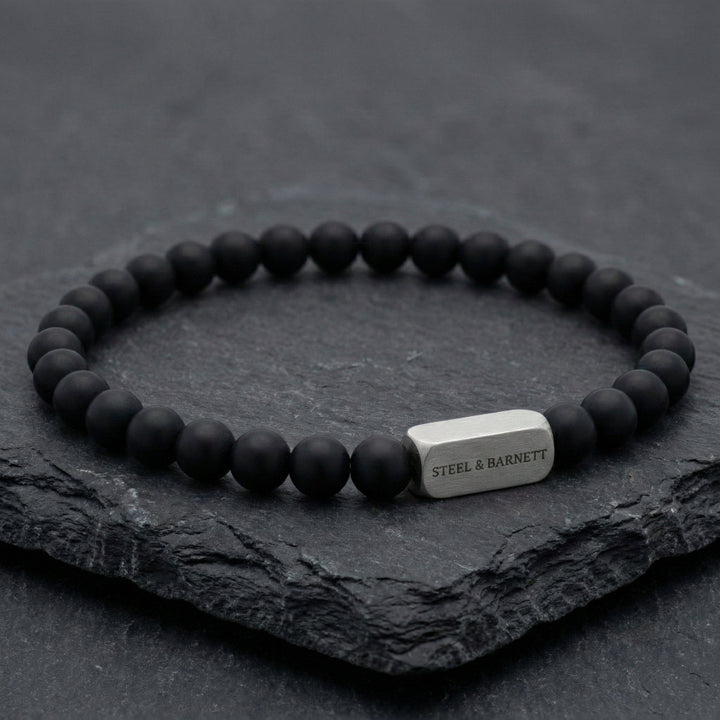 Black beaded bracelet with a silver tag on a dark stone surface