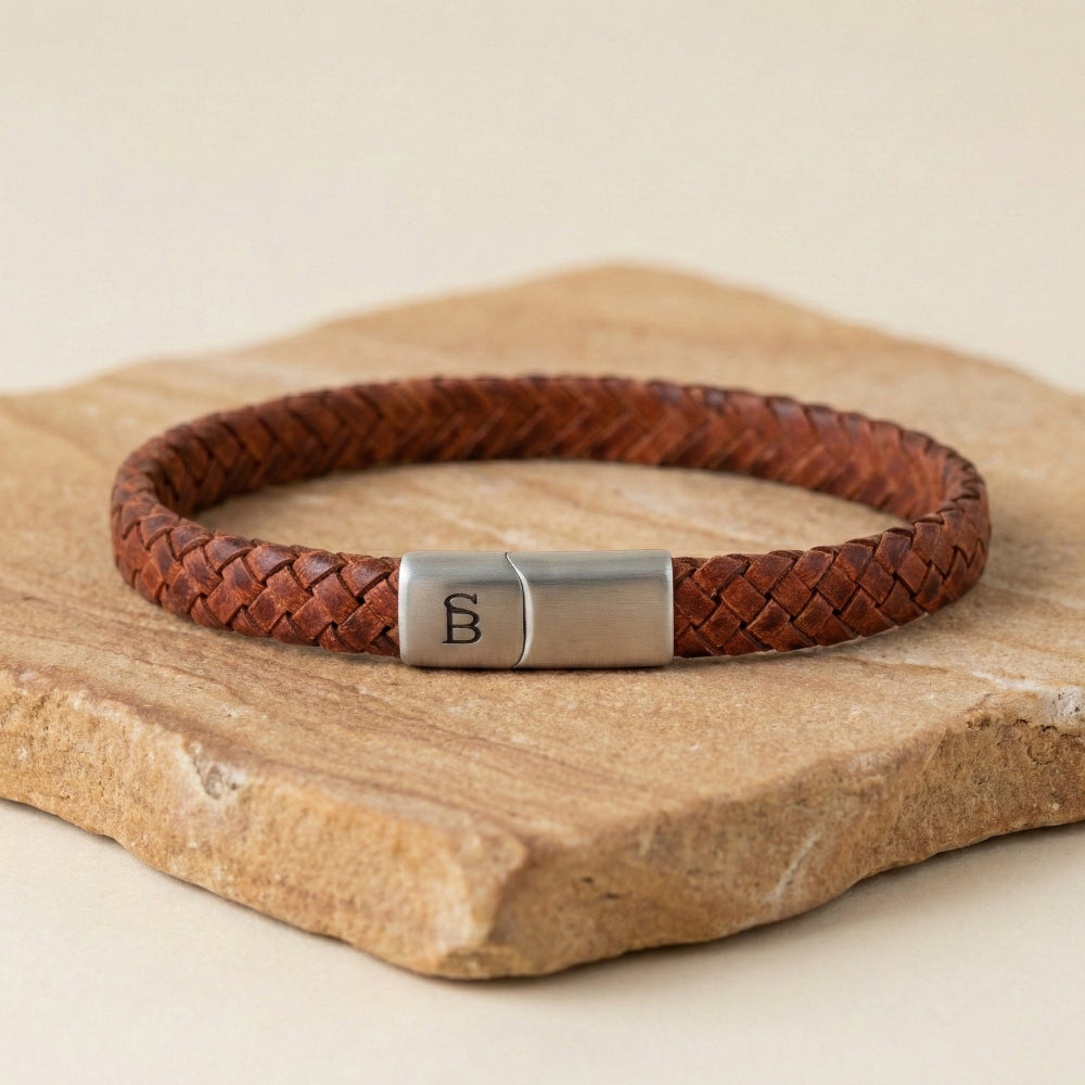Brown braided leather bracelet with a silver clasp on a wooden surface