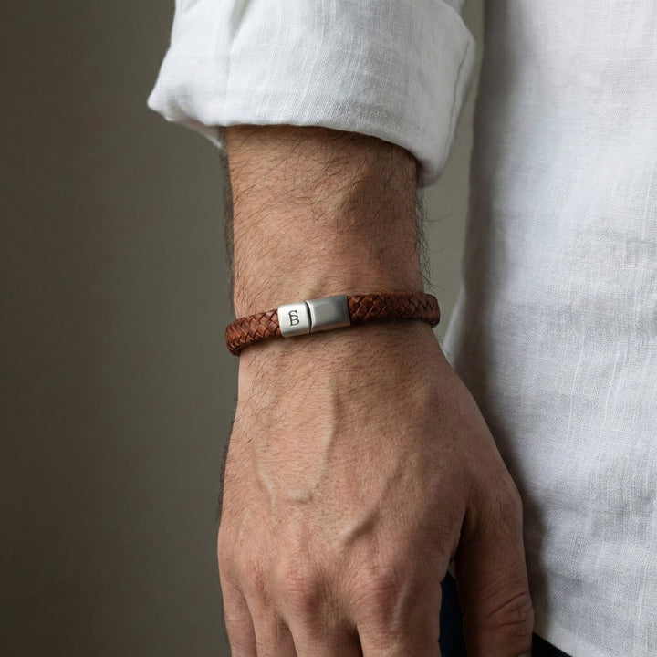 Brown leather bracelet with a silver clasp on a wrist against a neutral background