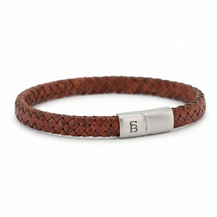 A brown braided leather bracelet with a silver-toned metal clasp engraved with the letter 'B', shown on a plain white background.
