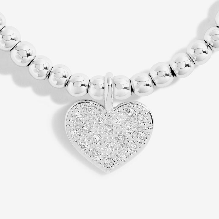 A close-up of a silver beaded necklace with a heart-shaped pavé pendant on a light gray background.