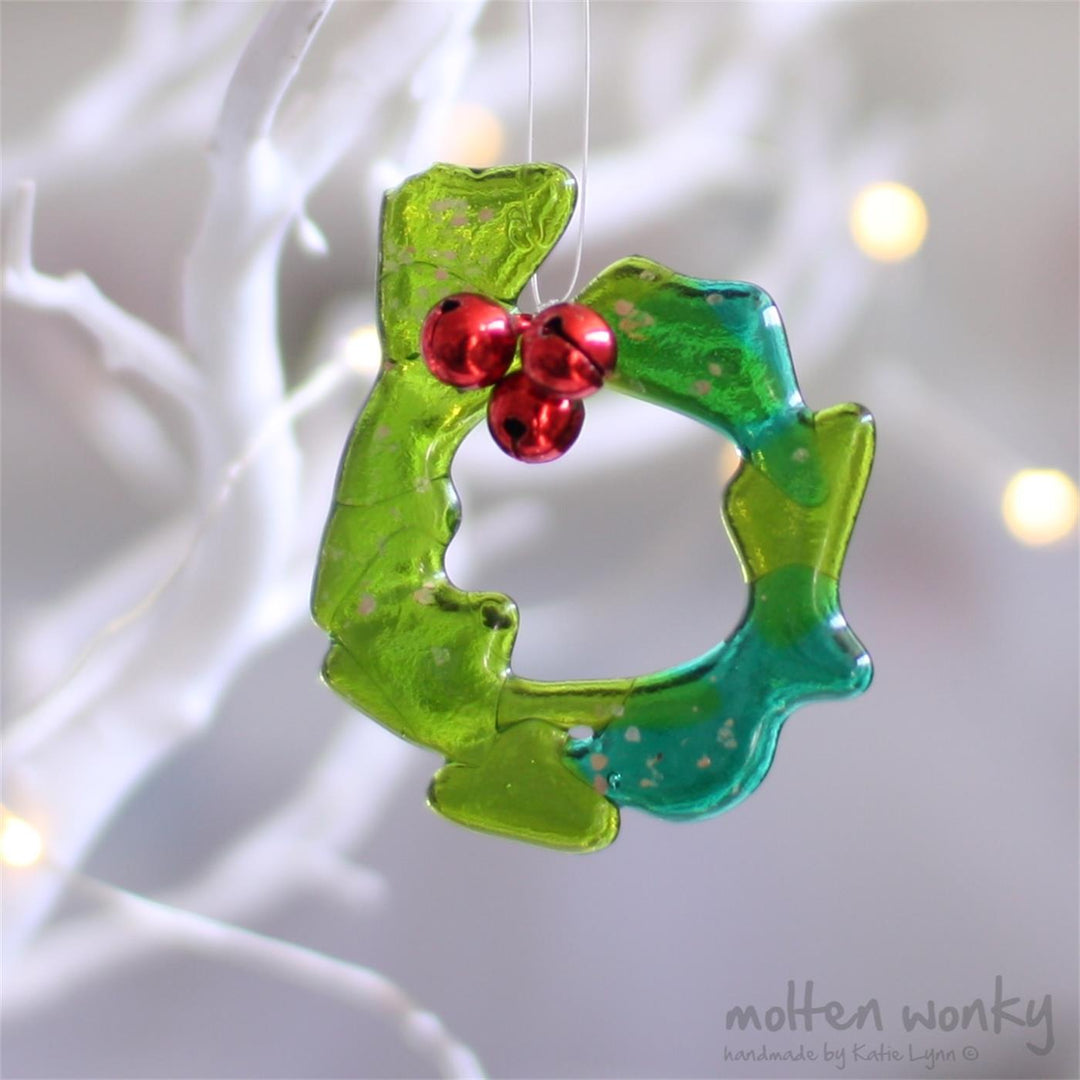 Fused glass wreath with green glass, gold glitter, and red bell details.